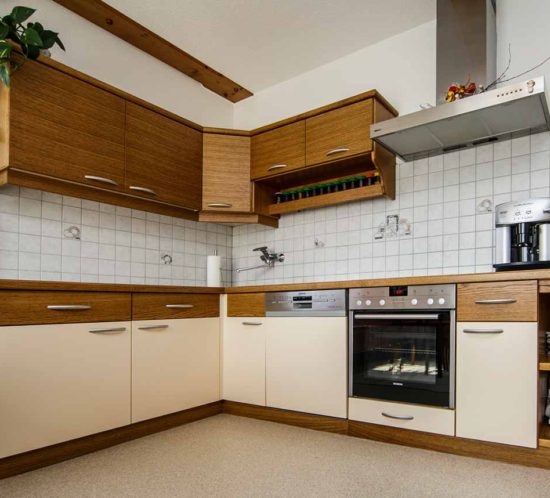 Küche mit Holz- und Creme-Fronten, Backofen, Dunstabzugshaube, Geschirrspüler und Gewürzablagen.