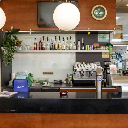 Café-Bar mit Kaffeemaschine, Flaschenregal und schwarzer Theke.