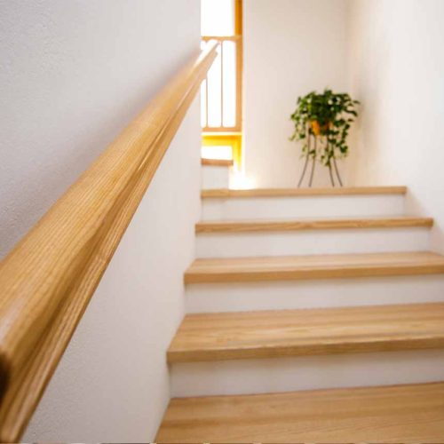 Holztreppe mit schlichtem Geländer und Pflanze im Hintergrund.