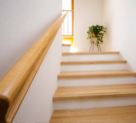 Holztreppe mit schlichtem Geländer und Pflanze im Hintergrund.