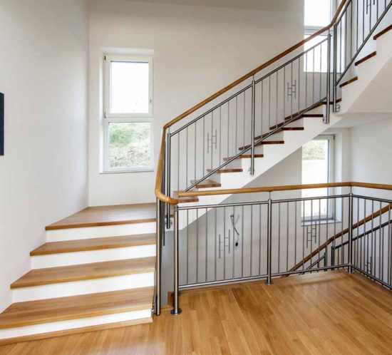 Holztreppe mit Metallgeländer und großen Fenstern.