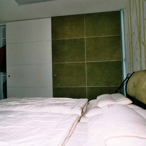 Großer Schrank mit Schiebetüren neben einem Doppelbett im Schlafzimmer.