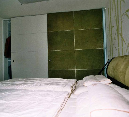 Großer Schrank mit Schiebetüren neben einem Doppelbett im Schlafzimmer.