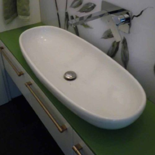 Ein ovale Waschschüssel mit grüner Arbeitsplatte und Wandleuchte im Hintergrund.