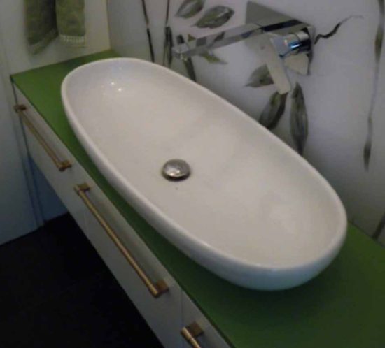 Ein ovale Waschschüssel mit grüner Arbeitsplatte und Wandleuchte im Hintergrund.