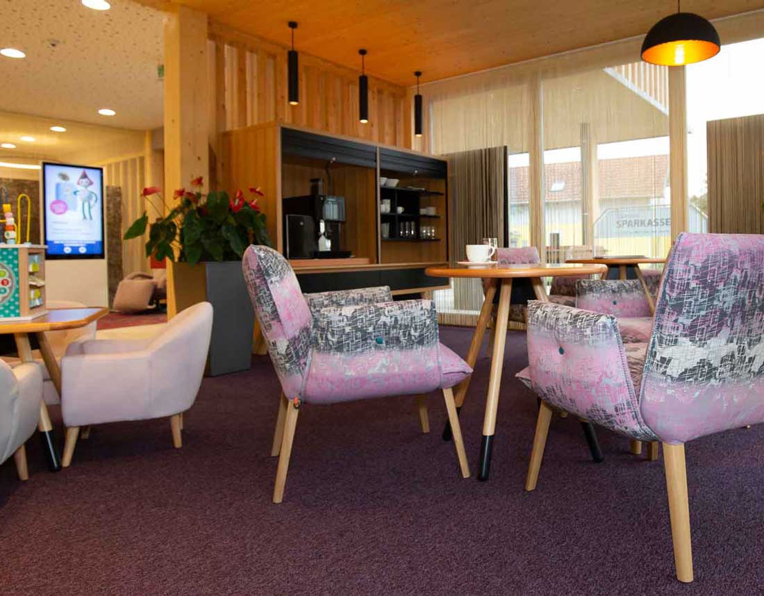Wartebereich einer Bank mit bequemen Sesseln, Kaffeestation und modernem Innendesign.