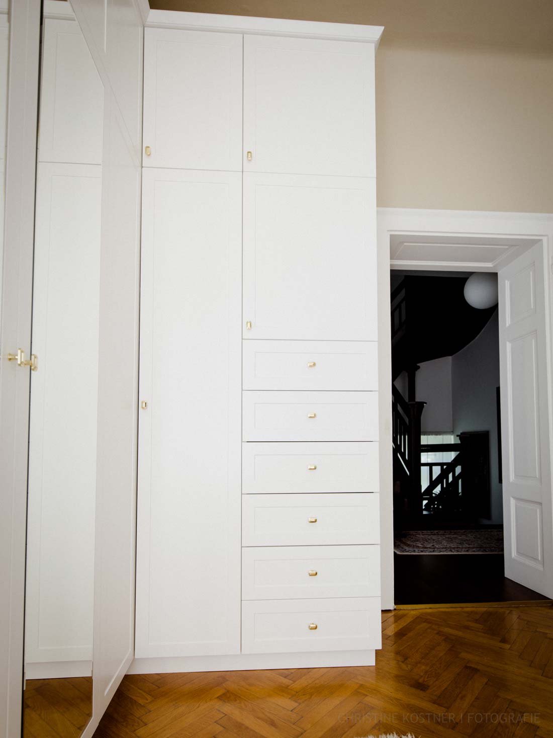 Weißer Einbauschrank mit Schubladen und goldenen Griffen vor einem hölzernen Fischgrätenboden.