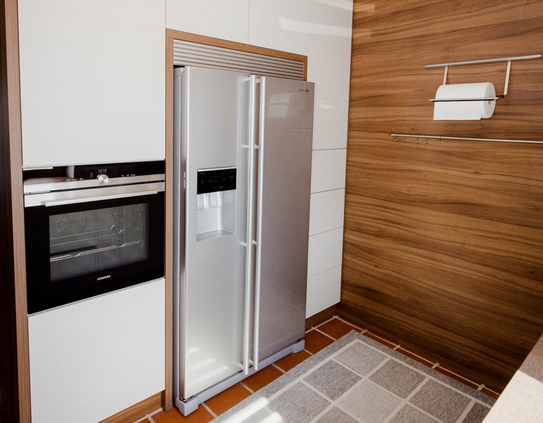 Küche mit Edelstahl-Kühlschrank, eingebautem Backofen und Holzverkleidung.