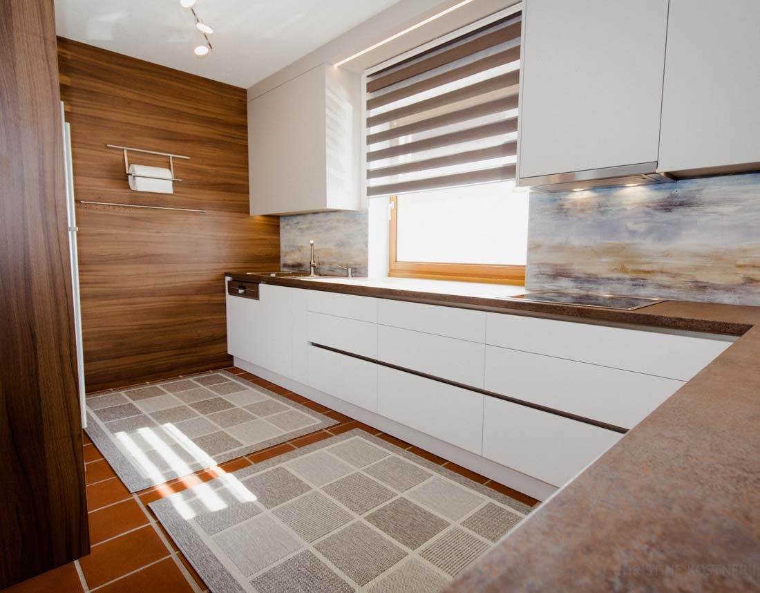Moderne Küche mit weißen Schubladen, Holzverkleidung, Terrakottafliesen und gemusterten Teppichen.
