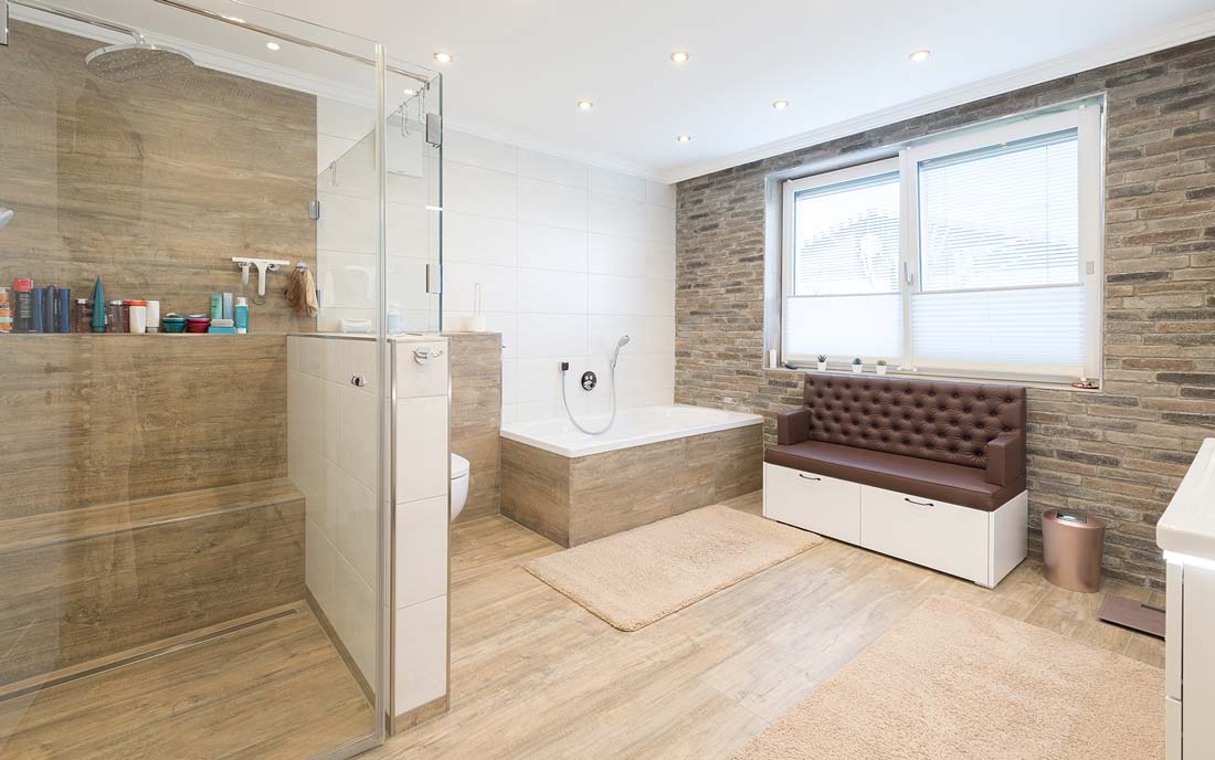 Großes Badezimmer mit begehbarer Dusche, Badewanne, gepolsterter Sitzbank und gemauerten Wänden.
