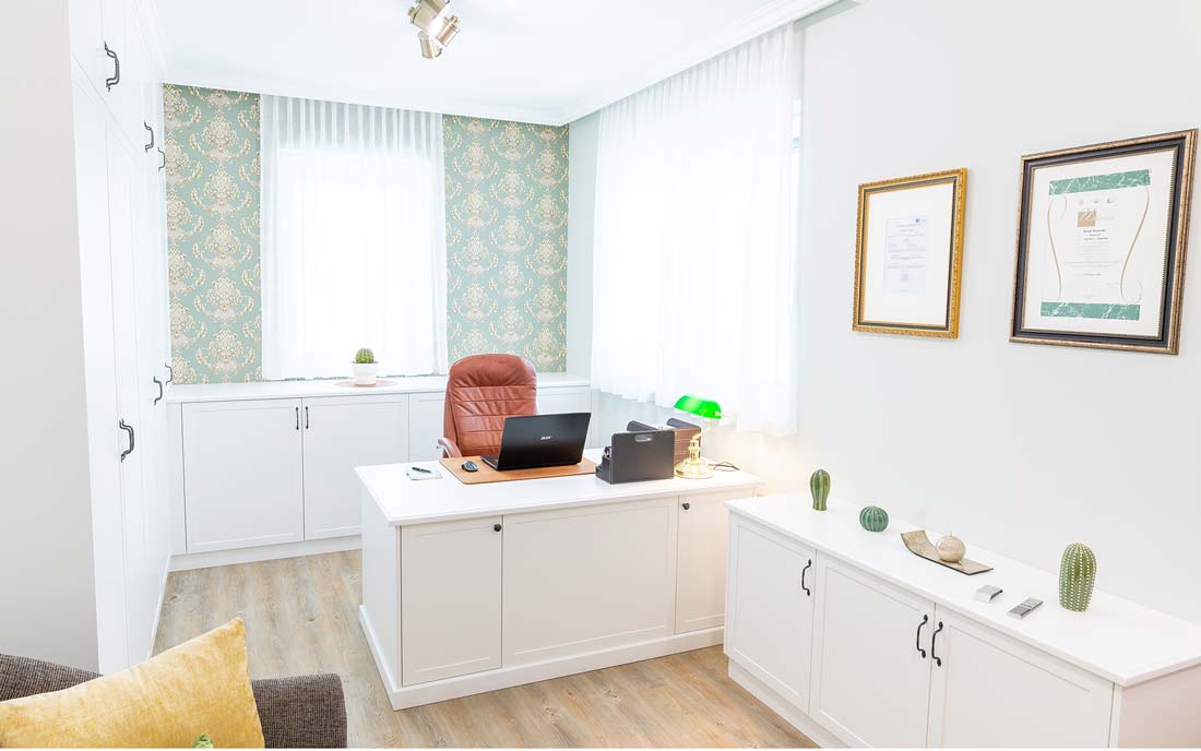 Helles Büro mit weißem Schreibtisch, Lederstuhl, grüner Schreibtischlampe und stilvollen Tapeten.