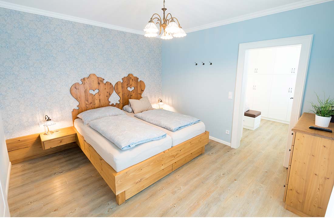 Schlafzimmer mit zwei Einzelbetten, rustikalem Holz-Kopfteil, blauen Wänden und Holzmöbeln.