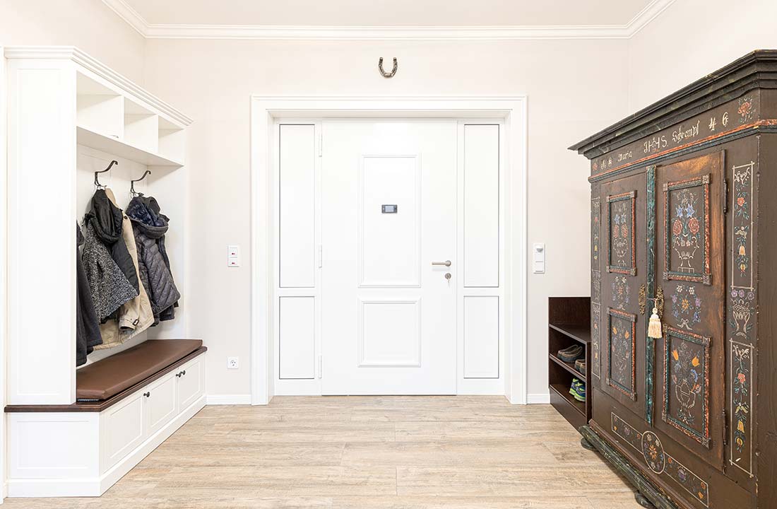 Eingangsbereich mit weißer Tür, Garderobe mit Sitzbank und dekorativ bemaltem Schrank.