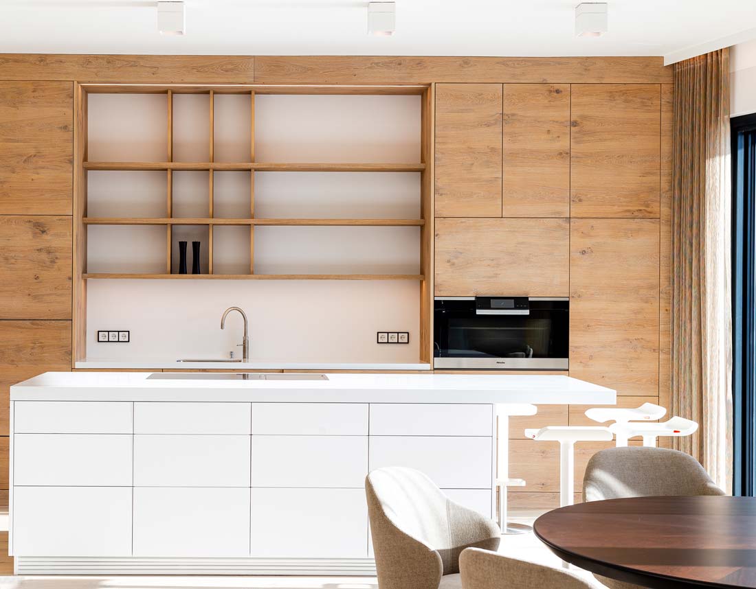 Moderne Küche mit weißer Insel, Holzverkleidung, Regalen, Einbauherd und minimalistischen Hockern.