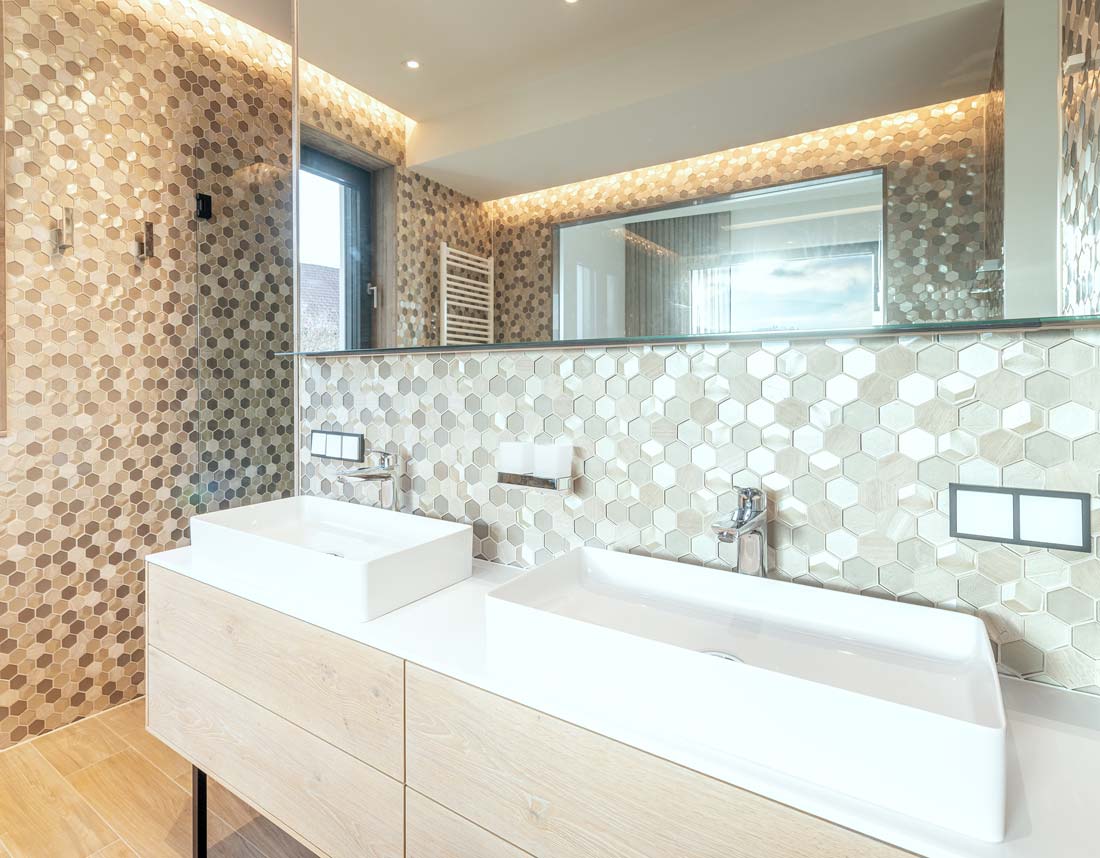 Modernes Badezimmer mit großen Spiegel, zwei rechteckigen Waschbecken und sechseckigen Mosaikfliesen an den Wänden.