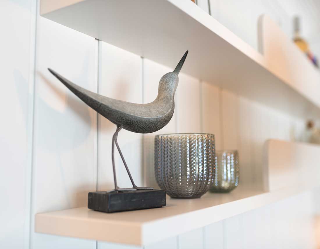 Nahaufnahme einer dekorativen Vogelstatue und Glasvasen auf einem weißen Regal.