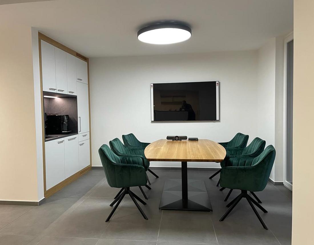 Moderner Besprechungsraum mit Holz-Besprechungstisch und grünen Stühlen.