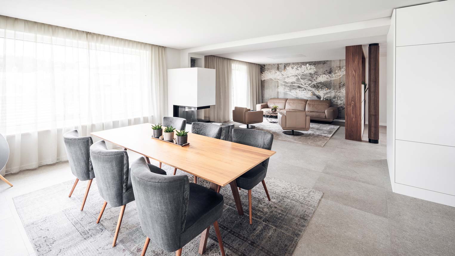 Helles Ess- und Wohnzimmer mit Holztisch und grauen Polsterstühlen.
