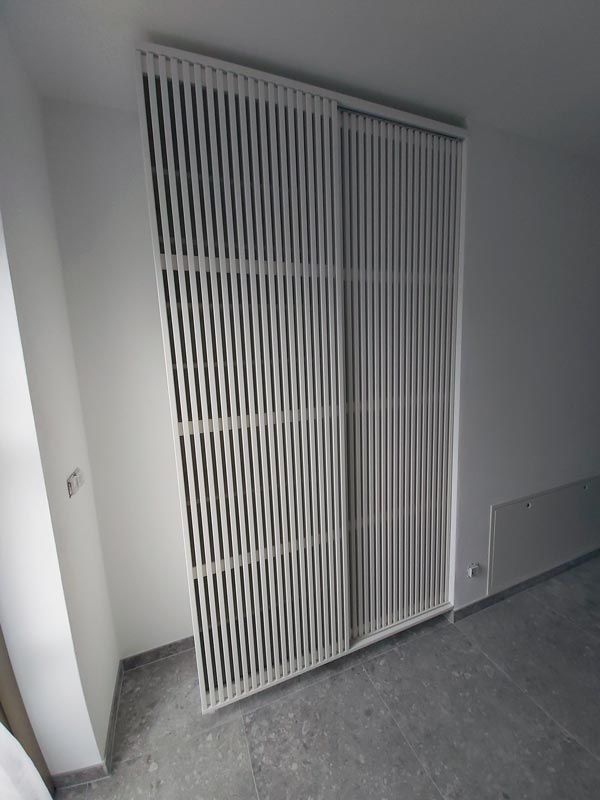 Weißer Schrank mit lamellenartigen Schiebetüren.