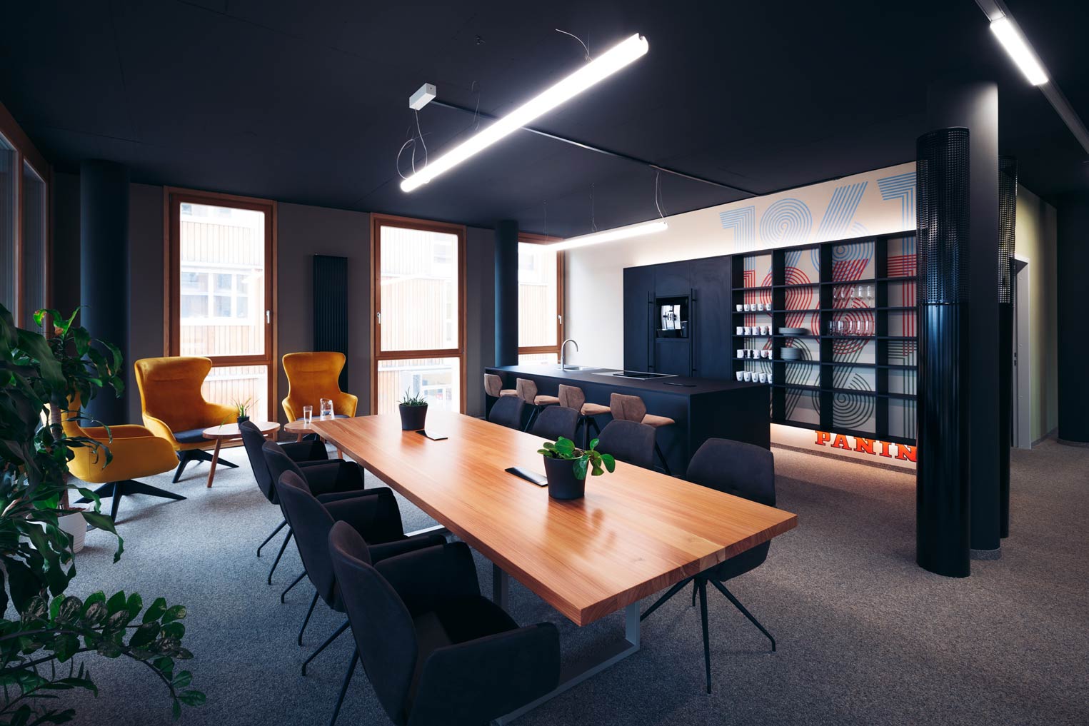 Ein modernes Büro mit einem großen Holztisch, gelben Sesseln und einer Küchenzeile im Hintergrund.