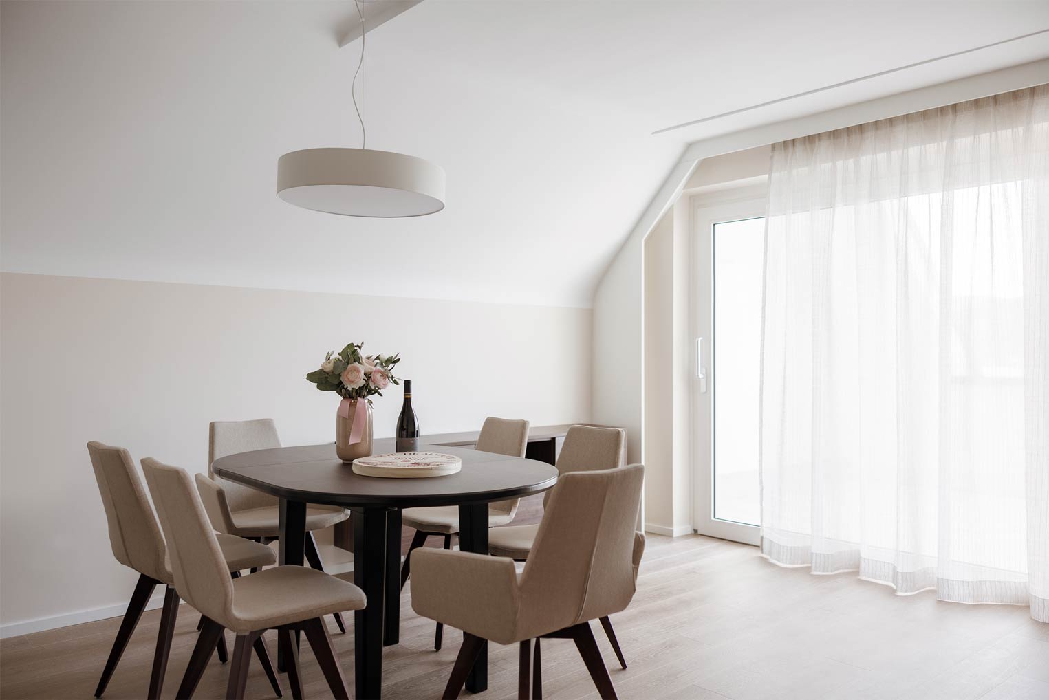 Essbereich mit rundem Tisch, sechs Stühlen und floraler Dekoration.