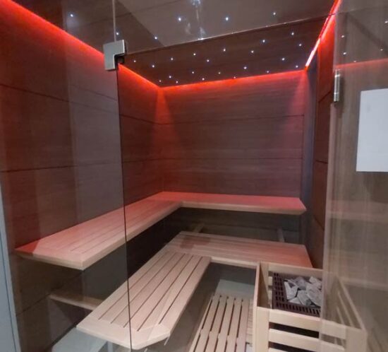Moderne Sauna mit Eckbänken, Holzverkleidung und roter LED-Beleuchtung