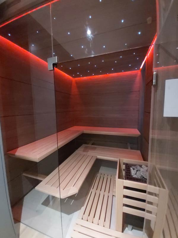 Moderne Sauna mit Eckbänken, Holzverkleidung und roter LED-Beleuchtung