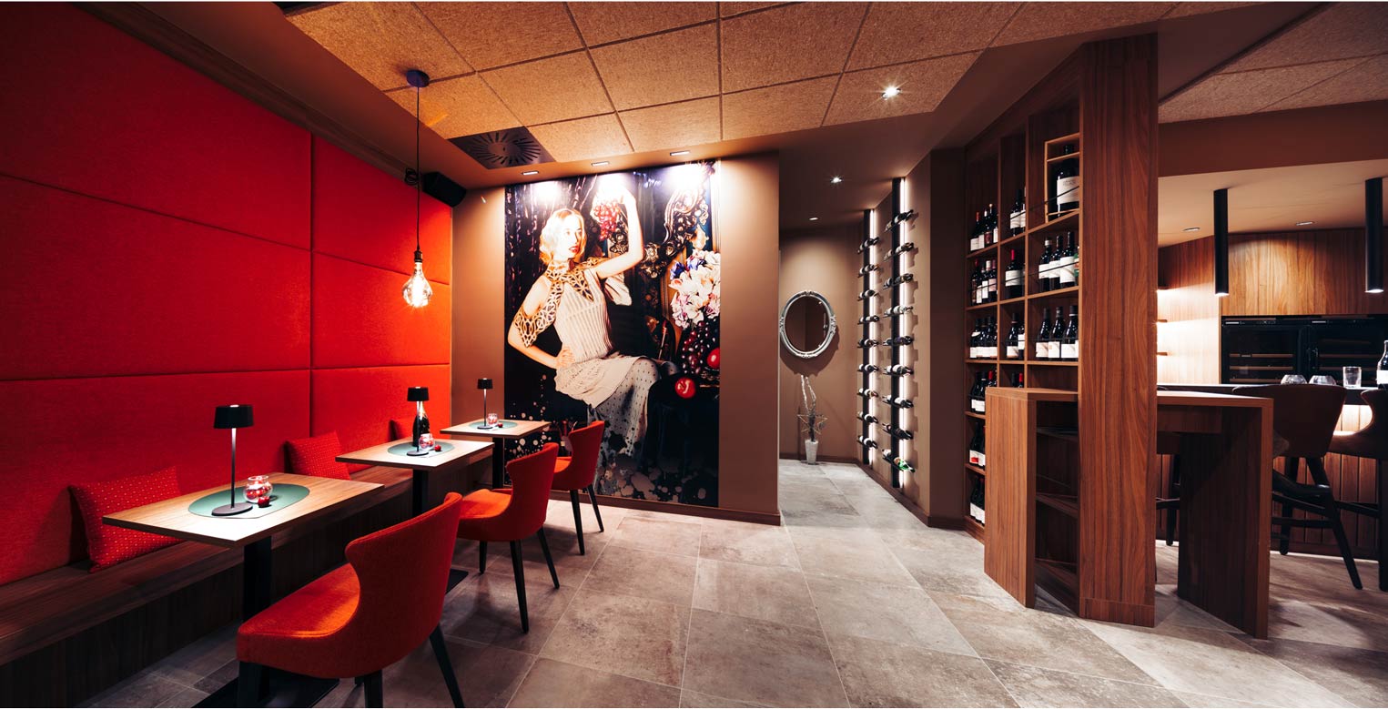 Stilvolle Weinbar mit roten Sitzecken, großer Wandillustration und Weinfächern aus Holz.